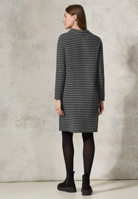 Gestreiftes graues Kleid mit langen Ärmeln, rundem Halsausschnitt und entspannter Passform, kombiniert mit schwarzen Knöchelboots und Strumpfhosen.