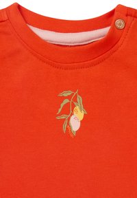 Rode katoenen t-shirt met een ronde halslijn, schouderknopen en een kleurrijke fruitillustratie aan de linkerzijde.