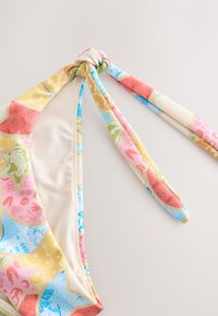 Meerlingkleurige bikinibovenkant met een knoopdetail. Heeft bloemen- en geometrische patronen in tinten roze, blauw, geel en groen. Verstelbare strikjes.