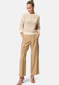 Knit beige sweater with open mesh pattern, paired with loose-fitting khaki cargo pants featuring side pockets and a smooth texture.