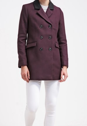 Dubbelzijdige jas van diep paarse wolmix, met een zwarte kraag, zes zwarte knopen en zijzakken, gecombineerd met witte broek.