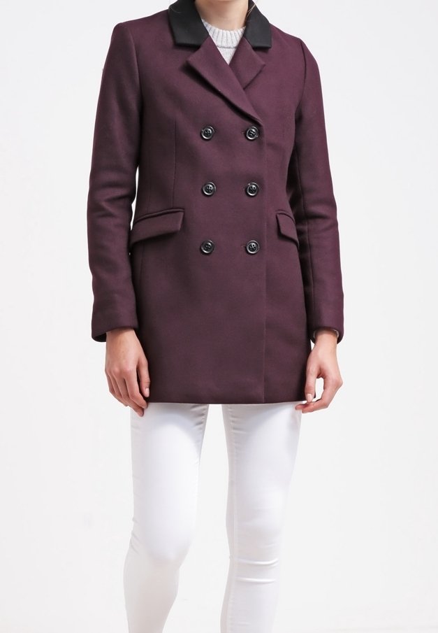 Dvojřadový kabát v tmavě fialové vlněné směsi, s černým límcem, šesti černými knoflíky a postranními kapsami, v kombinaci s bílými kalhotami.