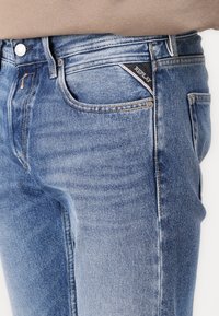 Blauwe denim jeans met een slanke pasvorm, lichte wassing, subtiele slijtplekken en een zwart stoffen merklabel op de voorzak.