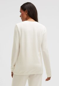 Weißes Langarmshirt mit einem strukturierten, gerippten Muster. Weicher Stoff mit rundem Ausschnitt und entspanntem Sitz, von hinten gezeigt.