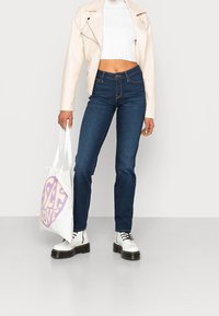 White cropped ribbed top, cream leather jacket, blue jeans, and white lace-up boots. Carrying a white tote bag with "SELF LOVE" in purple.