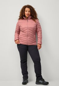 Lyserød quiltet jakke med høj krave, lynlås foran og elastiske manchetter, parret med sorte strækbukser og sorte vandrestøvler.