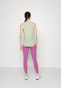 Atasan tanpa lengan berwarna hijau muda dipadukan dengan legging merah jambu. Atasan ini memiliki potongan yang longgar, sementara leggingnya pas di badan dan memiliki tekstur halus.