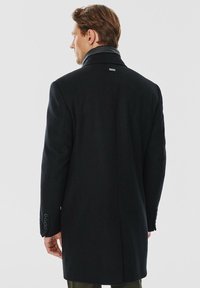 Czarny wełniany płaszcz o dopasowanym fasonie, z wysokim kołnierzem i gładkimi guzikami na rękawach, widziany z tyłu.