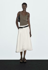 Tan tanktop en witte midi-rok met een zwarte riem. Zwarte handtas en bruine sandalen maken de look compleet. Eenvoudig, vloeiend ontwerp en kleuren.