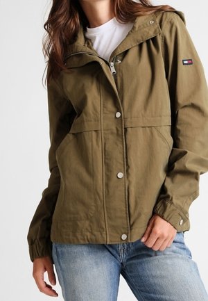 Olijfgroen, lichtgewicht jack met capuchon, drukknopen, elastische manchetten en twee voorzakken. Beschikt over een logopatch op de linkermouw.