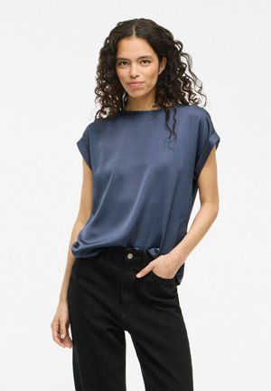 Top en soie bleu marine avec des manches courtes roulées, coupe décontractée et texture lisse, associé à un pantalon noir taille haute.
