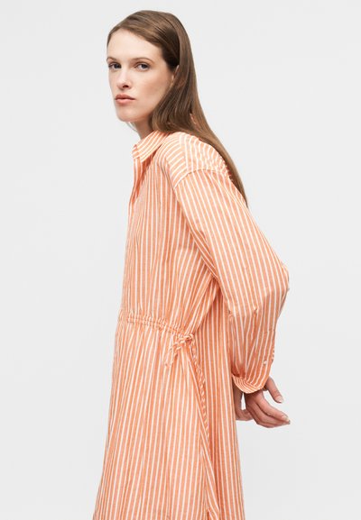 Φόρεμα με μακριά μανίκια σε ανοιχτό πορτοκαλί χρώμα με λευκές κάθετες ρίγες· διαθέτει γιακά και κορδόνι στη μέση για ρυθμιζόμενη εφαρμογή.
