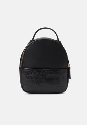 Sac à dos noir de forme arrondie. Doté d'un matériau supérieur lisse et d'un motif de crocodile texturé sur la partie inférieure. Détail de fermeture éclair doré.