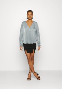 Blusa de cetim azul-claro com decote em V e mangas longas, emparelhada com uma saia mini preta justa com fendas laterais, usada com saltos pretos.