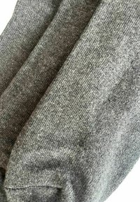 Nahaufnahme von drei gefalteten grauen Strickstoffstücken in unterschiedlichen Schattierungen und mit sichtbarer Textur, die Weichheit und das Strickmuster betonen.