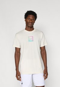 Ανοιχτό κρέμα κοντομάνικη μπλούζα με σχέδιο λογότυπου Asics σε μπλοκ χρωμάτων στο κέντρο του στήθους. Κατασκευασμένη από μαλακό και απαλό ύφασμα.