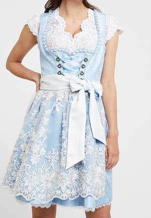 Woman wearing a light blue dirndl dress with white floral lace overlay, a wide white bow at the waist, and a white lace blouse underneath.