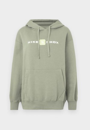 Zaļš krekls ar kapuci, kangaru kabatu, regulējamu aukliņu kapucē un baltu Nike Shox logotipu uz krūtīm. Gluds audums, brīva piegriezuma, ribveida aproces.