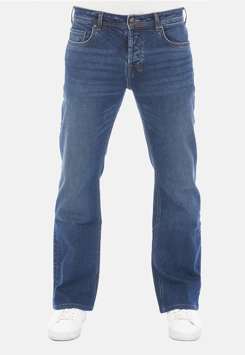 Jeans de mezclilla azul con corte recto, detalle desgastado, diseño de cinco bolsillos y costuras en contraste, combinados con zapatillas blancas.