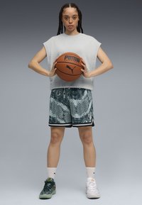 Gray oversized sleeveless shirt, green patterned shorts, holding a basketball. Footwear: green and white sneakers with contrasting details.