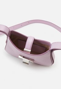 Lawendowa skórzana torebka o gładkiej fakturze, prostokątnym kształcie, srebrnych elementach metalowych i prostym zapięciu. Wnętrze wyposażone w dopasowany pasek.