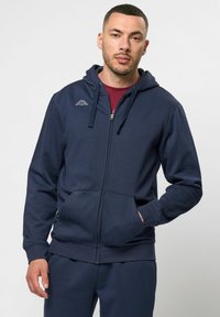 Tumes sinine lukuga kapuutsiga särk, mis on valmistatud pehmest kangast. Omab esiosa taskut, soonikkoes varrukaotsi ja väikest logo rinnal. Ühtlane sile tekstuur.