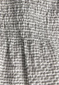 Biały materiał z czarnym wzorem kratki, marszczony i karbowany, tworzący poziome i pionowe fałdy.