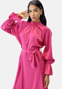 Vestido de satén rosa con cuello alto, mangas largas abullonadas y cintura atada. La tela tiene una textura suave y brillante.