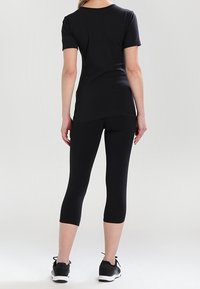 Svart kortärmad t-shirt och capri leggings i ett stretchigt material, med tajt passform och slät textur, parat med atletiska skor.