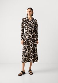 Abito con maniche lunghe e bottoni, in un motivo astratto nero e beige, con colletto e tasche, abbinato a sandali neri chunky.