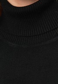 Pulôver de malha preto com gola alta e textura canelada, apresentando um design de gola alta e um acabamento suave, que acentua a elasticidade do tecido.