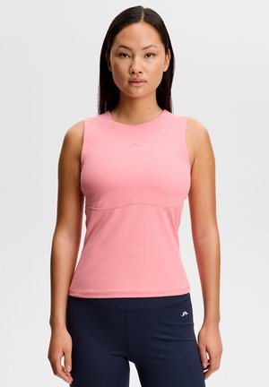 Vrouw die naar voren kijkt, gekleed in een mouwloos roze top en marineblauwe leggings met een klein wit logo op de borst en dij.