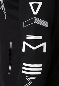 Tissu noir avec des formes géométriques blanches et des lignes abstraites disposées verticalement sur une manche.