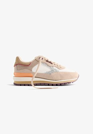 Sneaker beige et blanc avec un logo argent scintillant, semelle marron clair, détail de talon orange et lacet beige défait sur fond blanc.