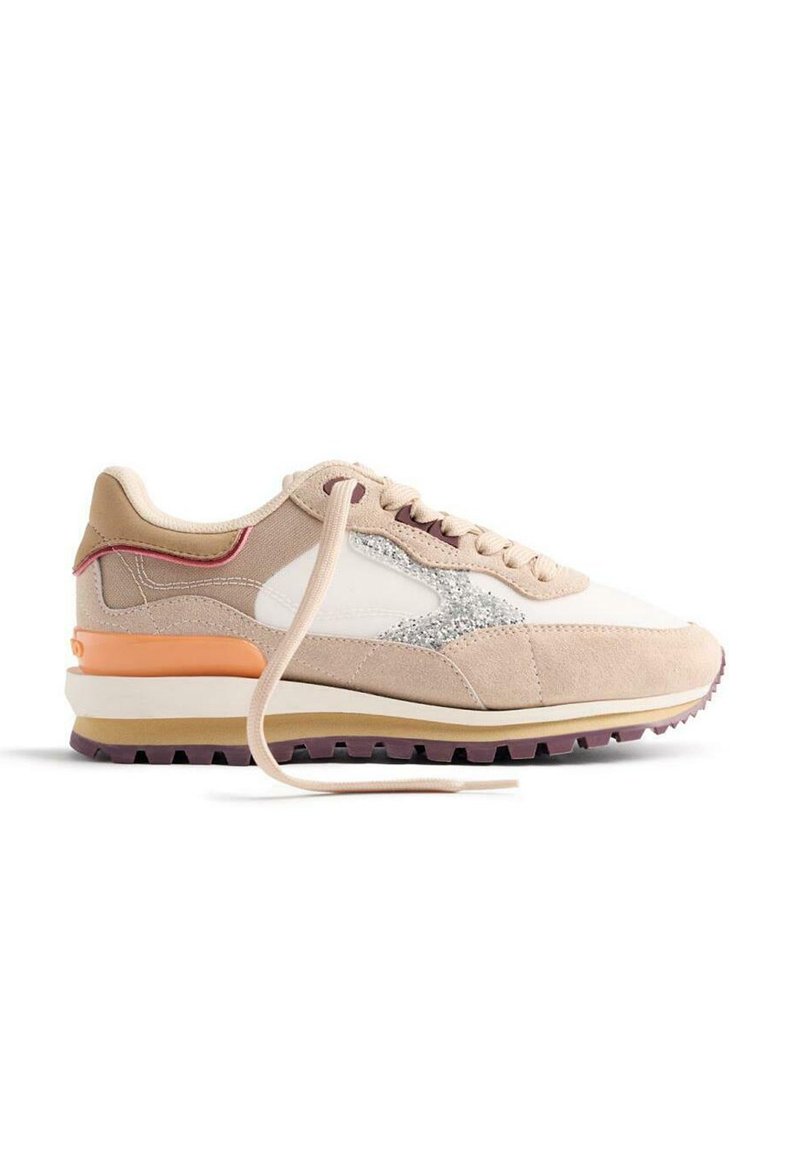 Sneaker beige et blanc avec un logo argent scintillant, semelle marron clair, détail de talon orange et lacet beige défait sur fond blanc.
