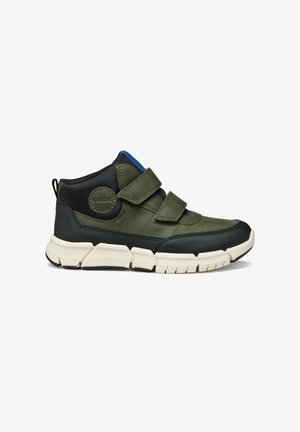 Zapatilla verde y negra con correas de Velcro, punta redondeada, upper texturizado y suela blanca acolchada. Presenta un detalle de logo circular.