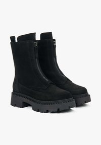 Zwarte suède enkelboots met dubbele zijritsen, chunky zwarte rubberen zool en verstevigde stiksels details bij de neus en zijkanten.