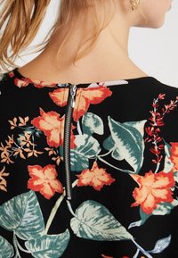 Robe noire à motifs floraux orange et verts. Dotée d'une fermeture éclair discrète à l'arrière. Tissu lisse et léger.