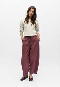 Pull en tricot crème avec finition texturée et manches tombantes ; pantalon ample bordeaux avec taille élastique et cordon de serrage ; chaussures noires.