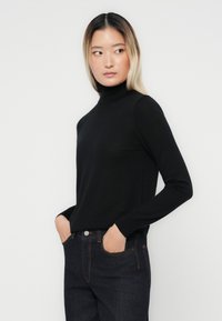 Pull noir à col roulé fabriqué dans un matériau doux, avec des manches longues et une coupe ajustée, associé à un jean en denim foncé.
