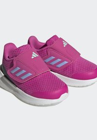 Zapatillas deportivas rosas con parte superior texturizada, correa de Velcro, suela blanca y tres franjas azul claro a un lado.