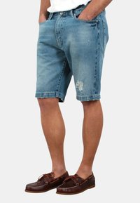 Shorts di jeans di colore blu chiaro con una finitura consumata, dotati di tasche laterali e un design a gamba dritta. Indossati con scarpe da barca in pelle marrone.