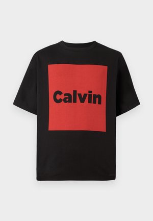 Camiseta de algodón negra con un cuadrado rojo audaz que lleva la palabra "Calvin" en una gran fuente negra. Mangas cortas y un cuello redondo clásico.