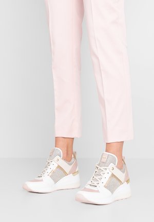 Pantalon rose clair longueur cheville associé à des baskets compensées blanches et dorées avec des détails en mesh et cuir.