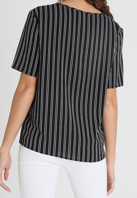 Haut à manches courtes rayé noir et blanc avec une coupe décontractée et un col rond ; présente des rayures verticales et une texture lisse.