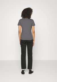 Szara koszulka z krótkim rękawem o okrągłym dekolcie, zestawiona z czarnymi spodniami prostymi i czarnymi trampkami za kostkę. Prosty design, bez wzorów.