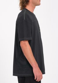 Zwarte T-shirt met korte mouwen en een relaxed fit, met contrasterende groene stiksels en een grafisch detail aan de zijkant. Zachte katoenfabricage.