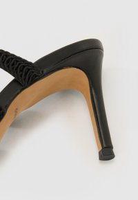 Sandalina nera con tacco alto, caratterizzata da una fascia testurizzata, parte superiore in pelle e tacco stiletto affusolato. L'interno presenta una fodera color sabbia.