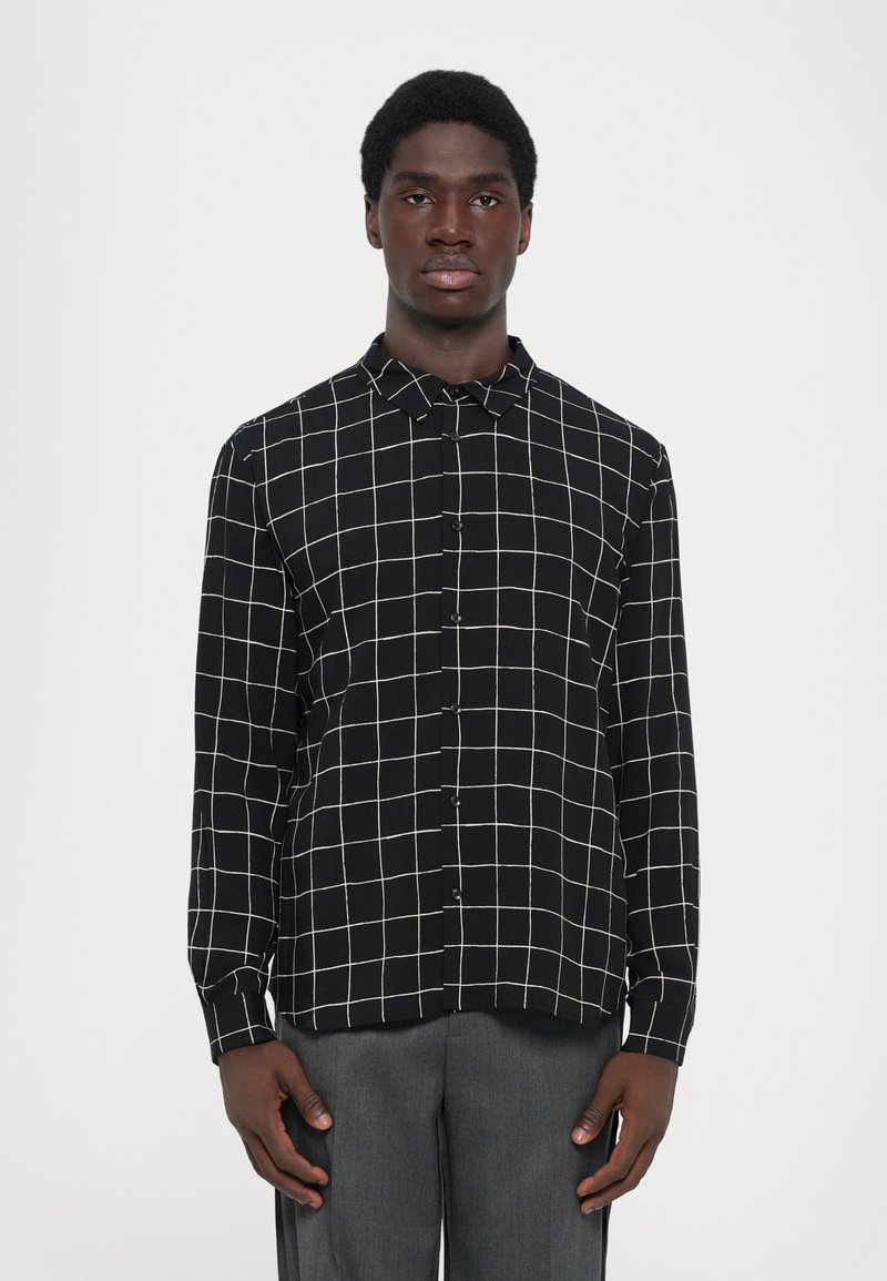 Heren overhemd met lange mouwen in zwarte stof met een wit ruitpatroon, voorzien van een kraag, knopenlijst aan de voorkant en een afgeronde zoom, gecombineerd met grijze broek.