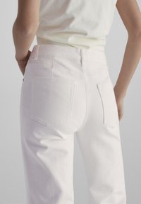 Witte denim broek met twee achterzakken en een soepele textuur. Heeft een middenhoogte taille en subtiele stikdetails langs de naden.